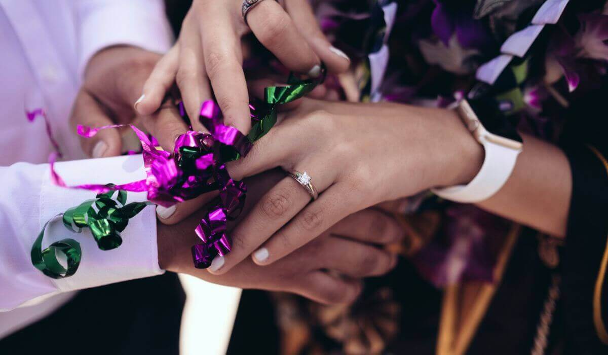 Hands intertwined with vibrant ribbons and a sparkling engagement ring, celebrating the engagement season.