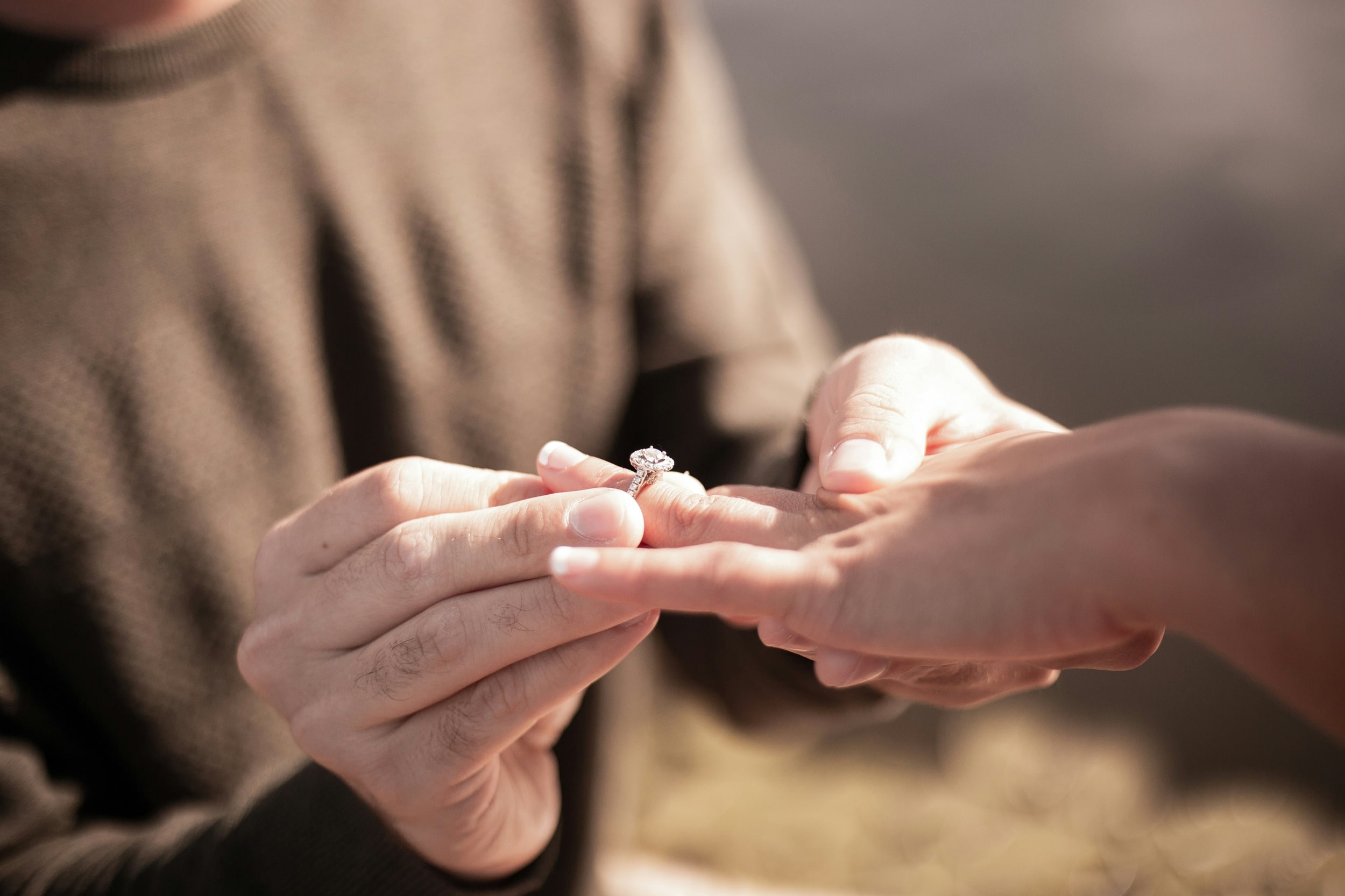 newly engaged couple in a field and the fiance puts the ring on his future wife's hand