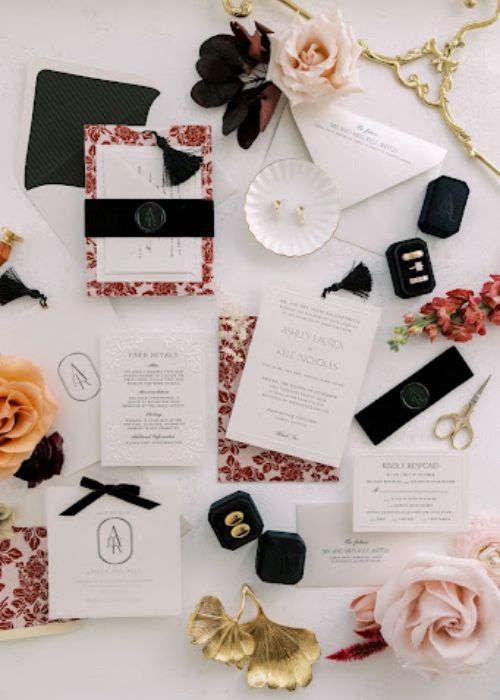 Flatlay photo of wedding essentials, including floral-patterned invitations, jewelry, and decorative elements arranged aesthetically on a neutral background.