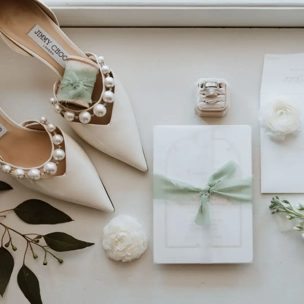 Elegant flatlay photos of pearl-adorned wedding shoes, invitation, and floral accents for a luxury wedding.