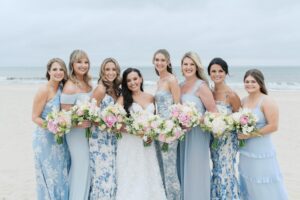Bridesmaids in pastel patterned dresses standing together on the Hamptons beach during this luxury coastal wedding.