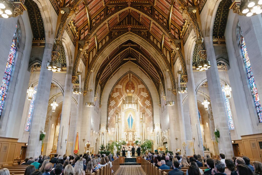 Ornate cathedral wedding ceremony with gold ceiling, stained glass, and full guest seating