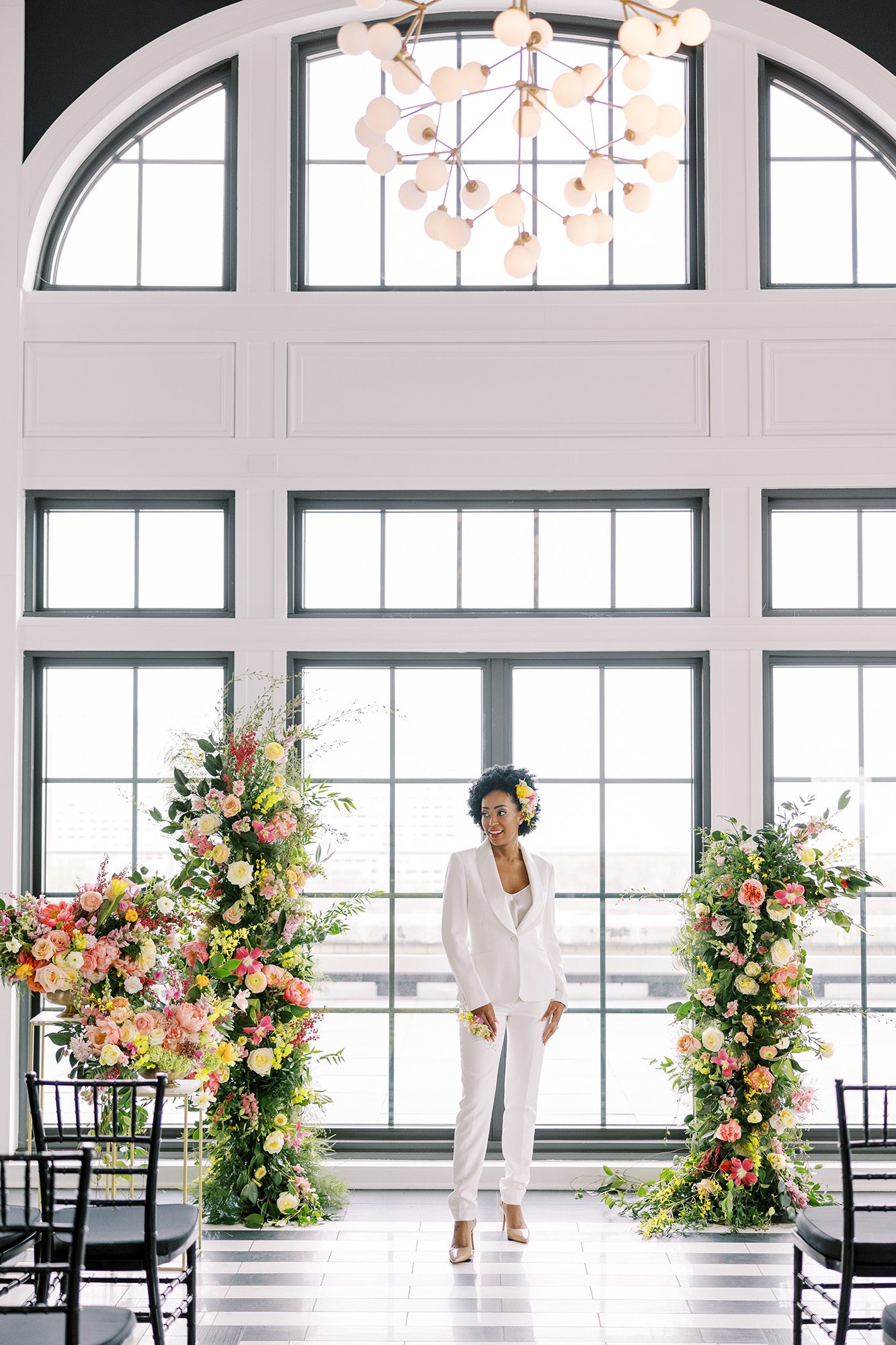 Stylish indoor wedding ceremony featuring bold floral arrangements, black chairs, and arched windows — curated by our full service wedding planning team in Chicago