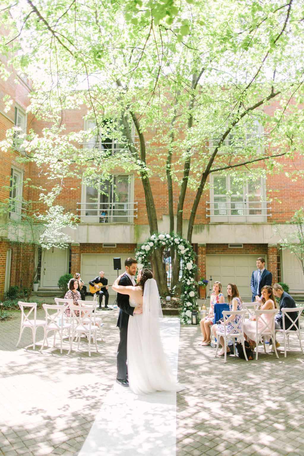 Couple dances under trees at their courtyard micro wedding with floral arch and live music