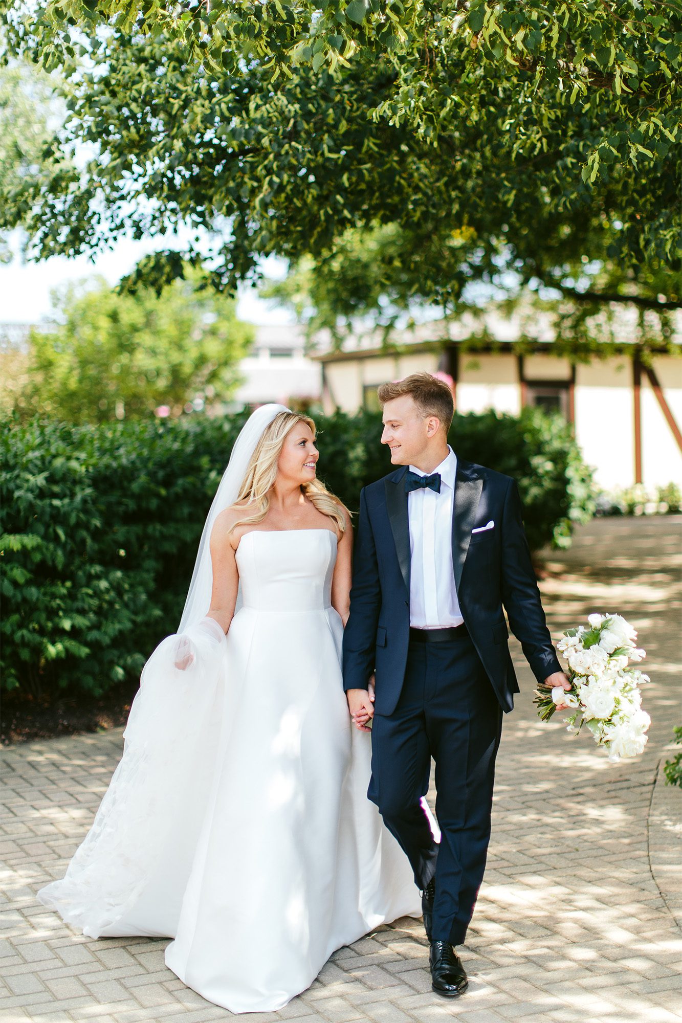 Bride and groom walk hand-in-hand through a lush outdoor path