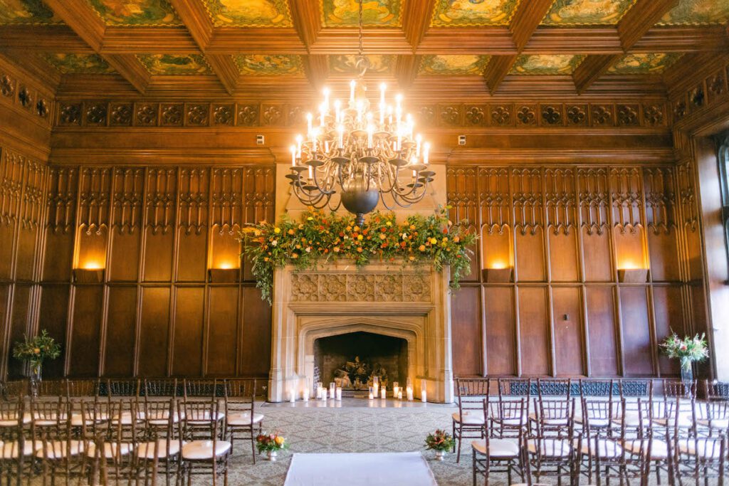 Michigan Room wedding with wood-paneled walls, floral fireplace, chandelier, and candlelit ceremony aisle.