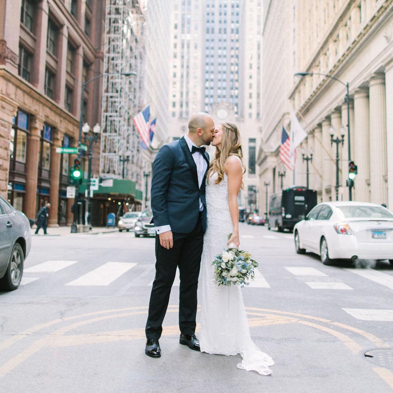 Wedding couple kissing on Chicago street with city buildings and flags in the background.
