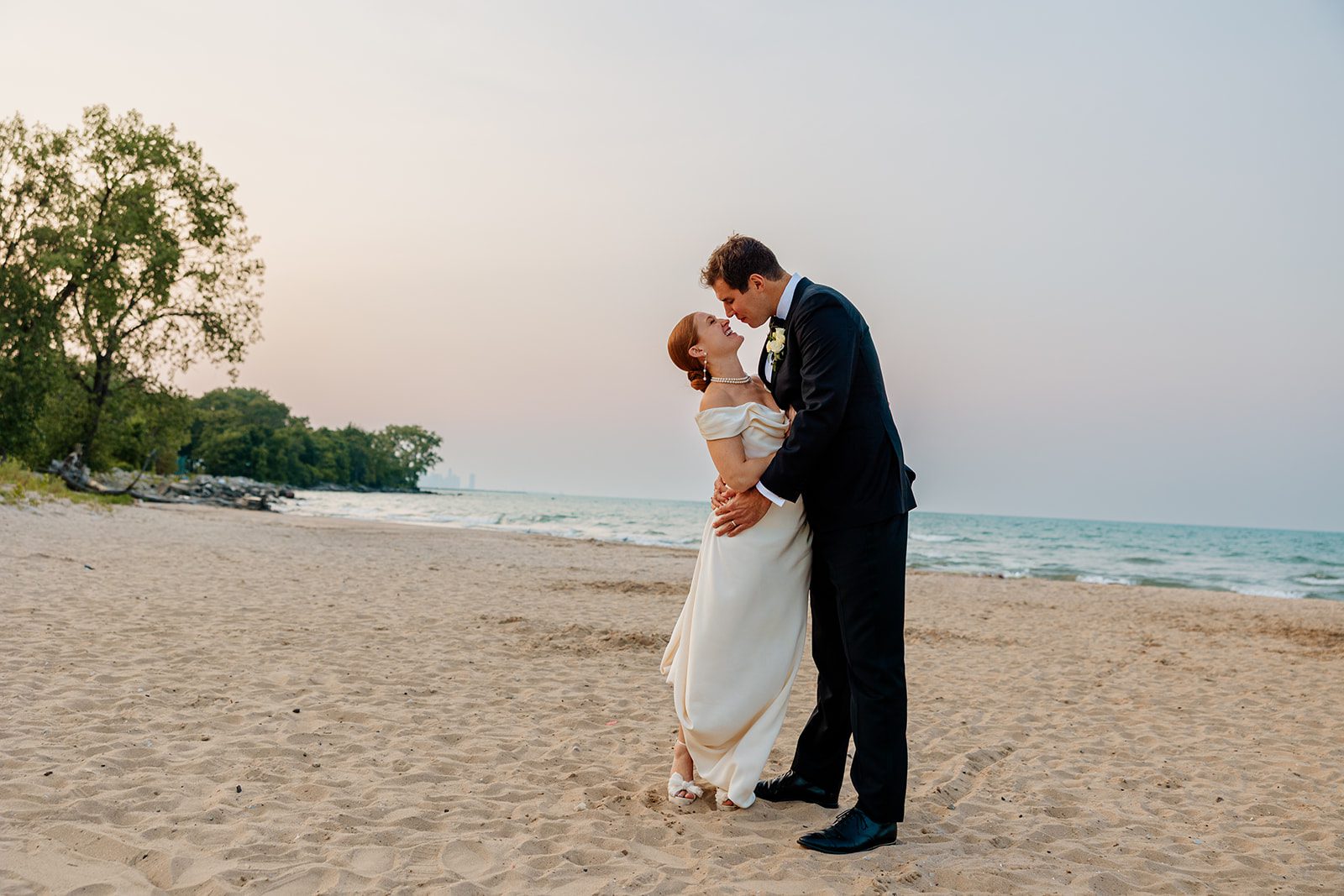 A couple embraces on a sandy beach near Chicago’s lakefront at sunset, dressed in elegant wedding attire. The romantic shoreline moment captures the essence of beach weddings in Chicago.