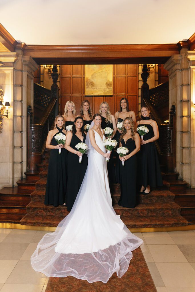 Bride and bridesmaids on grand staircase at historic chicago wedding venue with wood paneling and white bouquets.