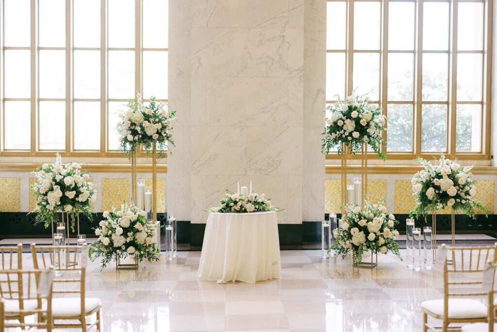 Symmetrical ceremony setup in the Historic Lobby featuring blush and white florals, gold stands, and floating candles.