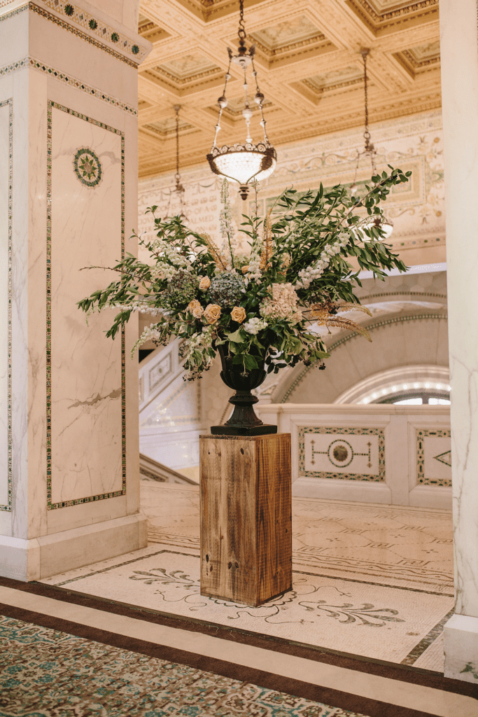 Grand floral arrangement on a pedestal in the Rotunda, surrounded by mosaic columns and chandeliers at the Chicago Cultural Center.