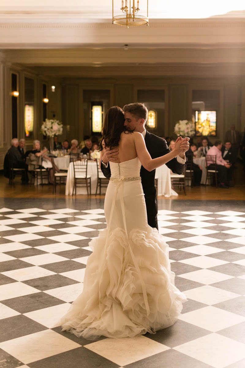 Bride and groom sharing their first dance on the Chicago History Museum’s black and white checkered ballroom floor surrounded by candlelit tables and white floral décor.