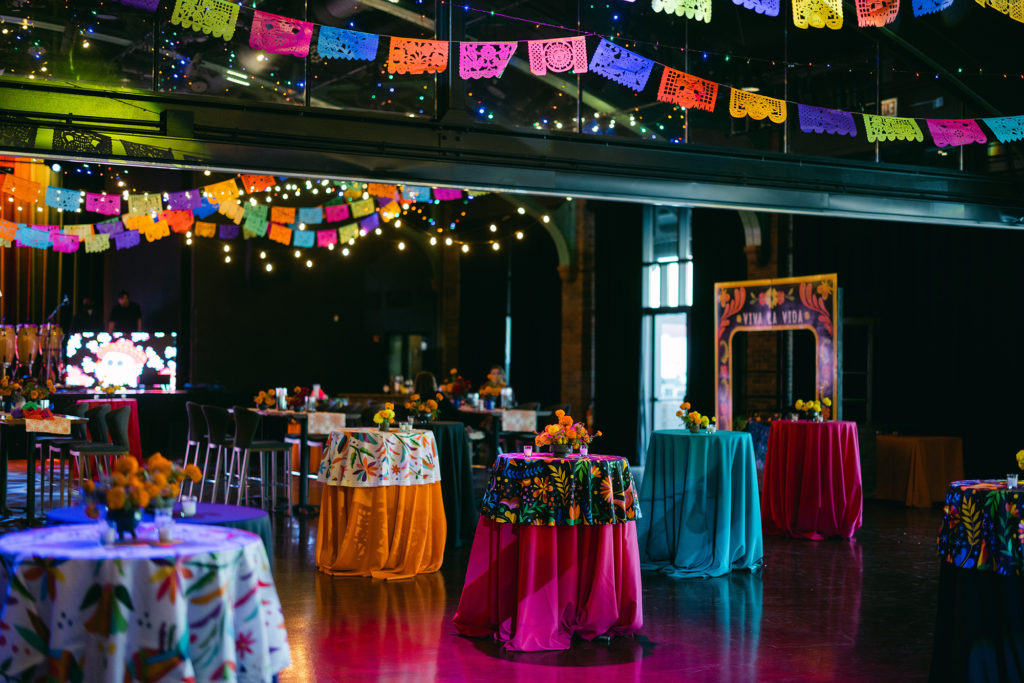 Vibrant indoor event space with colorful papel picado, floral tablescapes, and “Viva La Vida” archway for a festive holiday celebration.