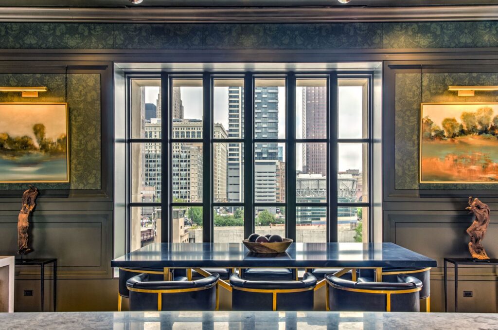 Elegant dining room with skyline views, sculptural wood art, and abstract paintings flanking a panoramic window at the Old Post Office.