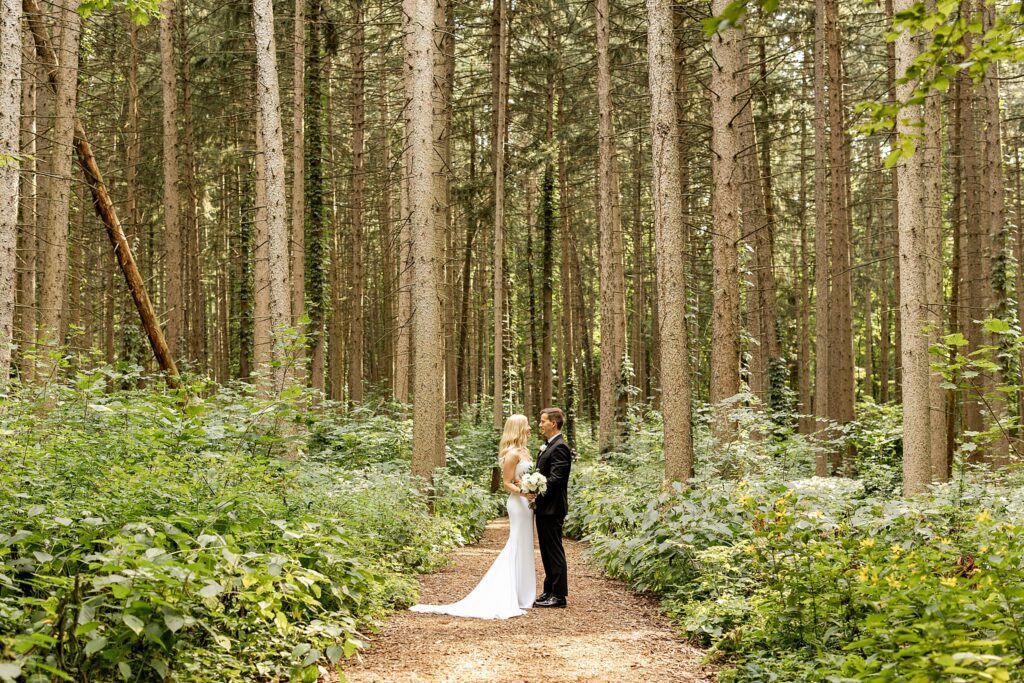 Couple standing on a forest path in the East Side Woods at Arboretum, surrounded by towering trees and lush greenery in a serene, romantic setting