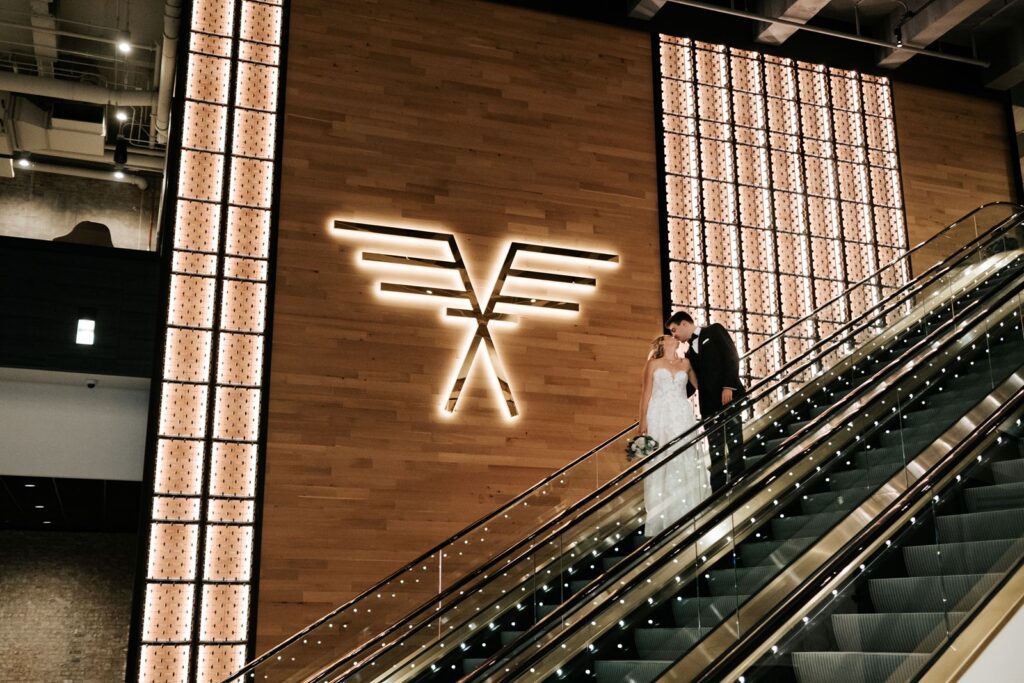 Romantic first look captured on the escalator at The Old Post Office, framed by architectural lighting and wood paneling.