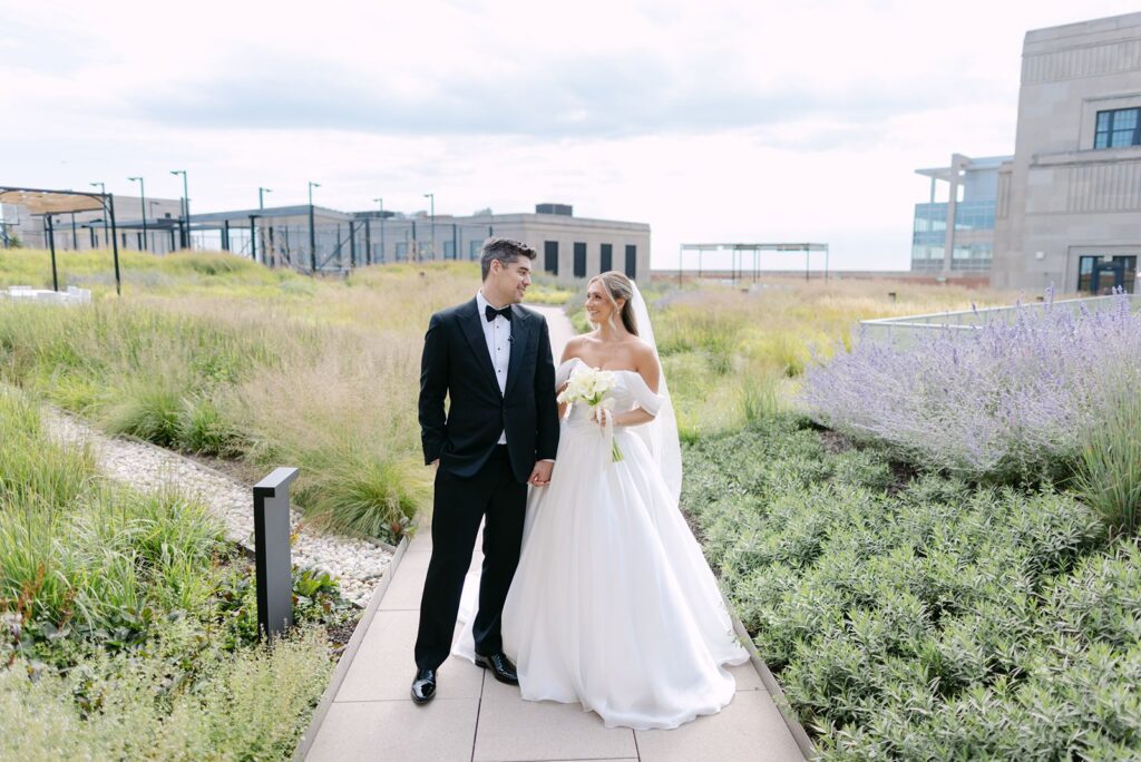 Bride and groom walk through The Meadow rooftop garden at The Old Post Office, surrounded by lavender and skyline views.