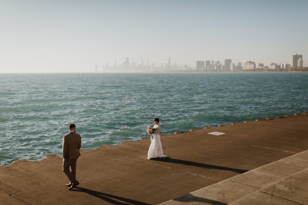 Couple walking on the sand at Montrose Beach under a clear blue sky, with a sailboat on the horizon.