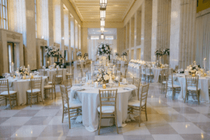 Luxurious Old Post Office Chicago wedding reception featuring gold Chiavari chairs, white and blush floral centerpieces, marble columns, and soaring ceilings