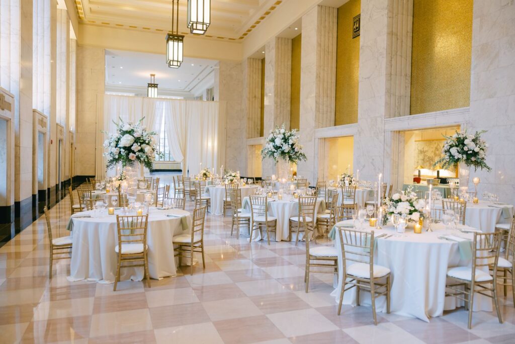 Reception tables with white linens, gold chairs, and lush florals set beneath lantern lights in The Old Post Office.