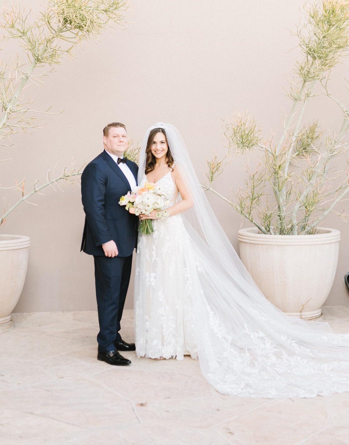 Bride and groom pose in Scottsdale wedding portrait with potted plants and neutral backdrop.