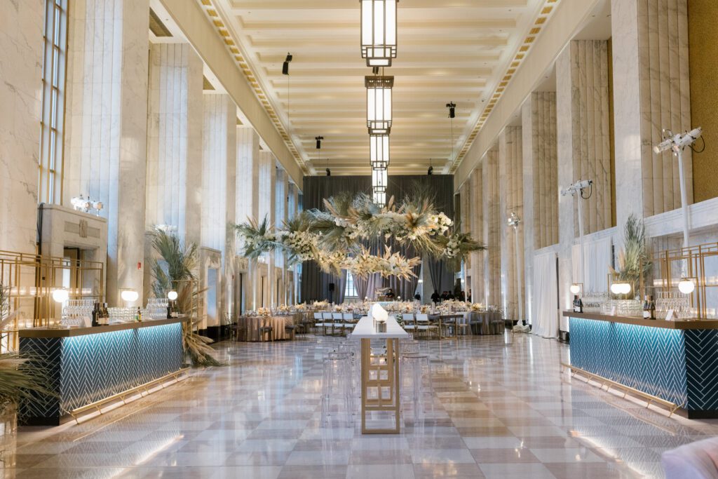 Luxurious wedding reception with hanging white florals and pampas grass, dark linens, candlelit tables, and marble walls at Chicago’s Old Post Office.