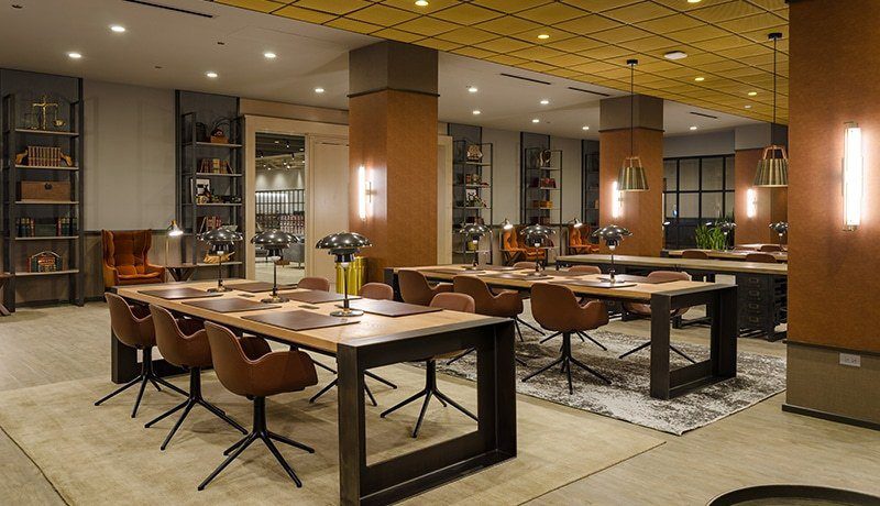 Modern library‑style lounge at the Old Post Office featuring long wooden tables, leather chairs, built‑in bookshelves, and warm pendant lighting.