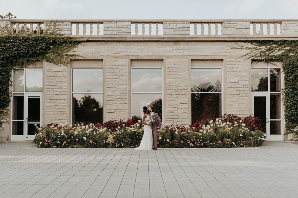 Couple standing in front of the ivy-covered Thornhill Education Center, framed by colorful garden blooms and classic stone architecture