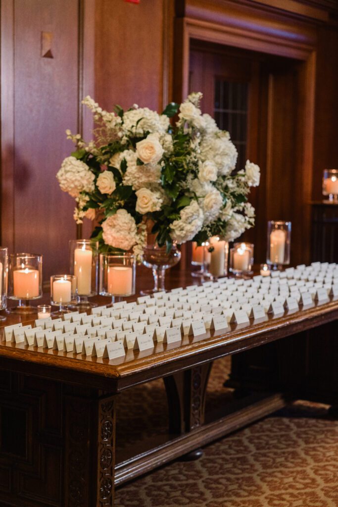 Escort card table with white florals, candles, and organized seating cards on wood table.