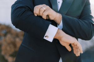 Groom adjusting a black tuxedo with satin lapels and cufflinks, illustrating black tie attire for the Wedding Dress Codes Explained guide.