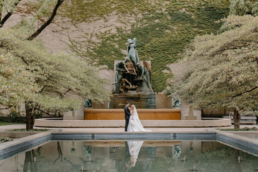Bride and groom portrait in the Art Institute of Chicago garden courtyard with reflecting pool and ivy-covered walls.