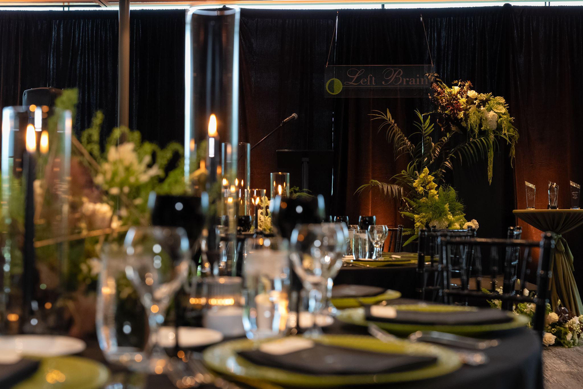 Branded presentation stage with dramatic florals and candlelit tables for a corporate anniversary celebration