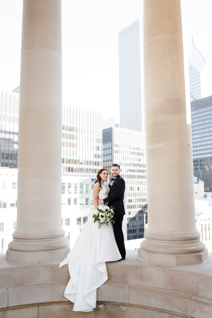Bride and groom posing between the iconic columns at LondonHouse Chicago with downtown skyline views during their rooftop wedding.