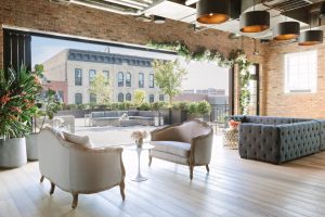 Indoor-outdoor Chicago lounge with tufted seating, floral garlands, and exposed brick for stylish social events.