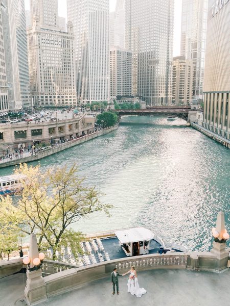 Bride and groom standing on Chicago River terrace with boat and skyscrapers behind them, capturing a romantic city wedding moment