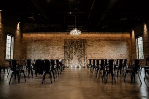 Industrial Chicago wedding ceremony with exposed brick, floral altar, and candlelit aisle under a chandelier.